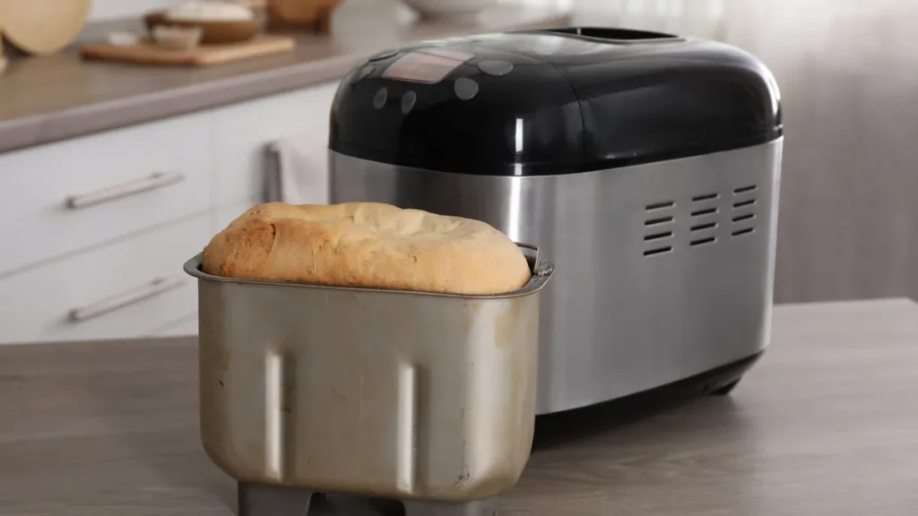 Pain de mie fraîchement cuit posé devant une machine à pain électrique en inox, sans marque visible, dans une cuisine